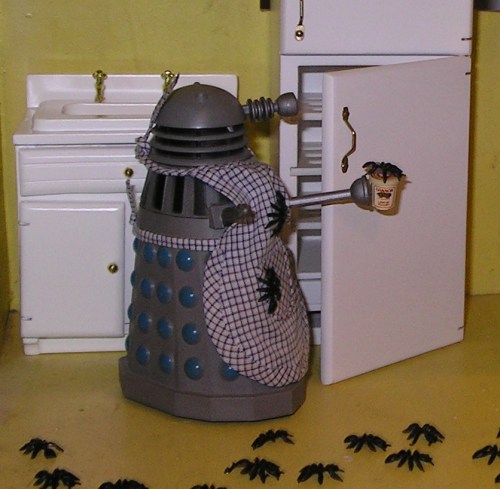 A Dalek stands in the kitchen of my dollhouse, wearing an apron and holding a jar of yogurt. Ants cover the floor and are climbing up its apron to get at the yogurt.